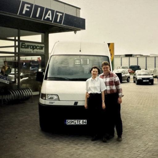 Paar vor weißem Fiat-Transporter vor einem FIAT-Autohaus – Symbol für die ersten Schritte nach der Gründung.